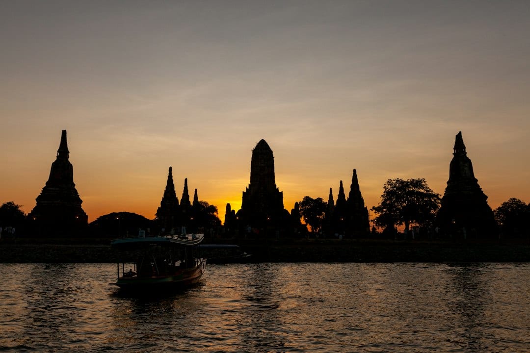 Temples silhouetted against a vibrant sunset over water during an Ayutthaya river cruise