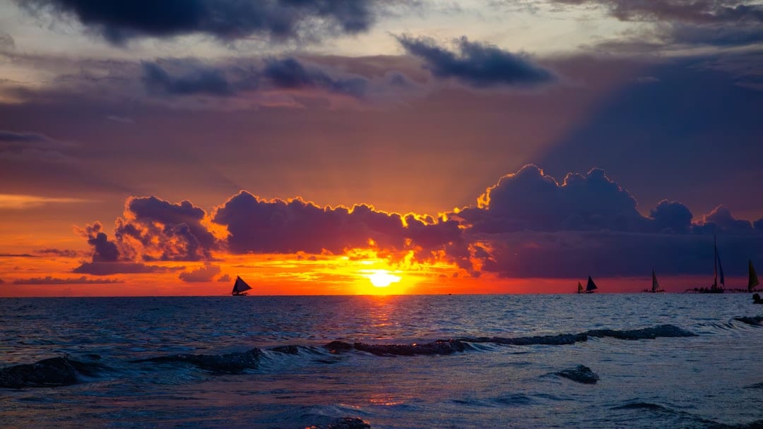 Boracay White Beach at sunset with traditional paraw sailboats on the horizon