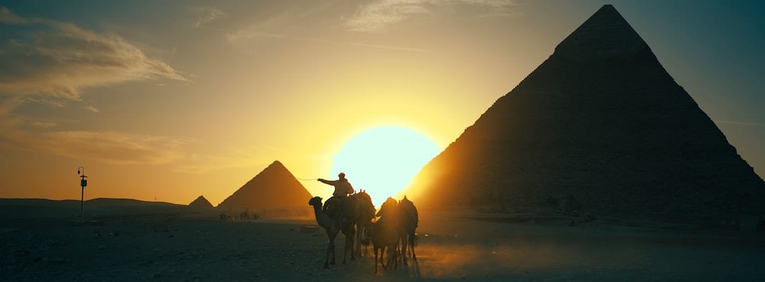 Camel caravan silhouetted against pyramids at sunset