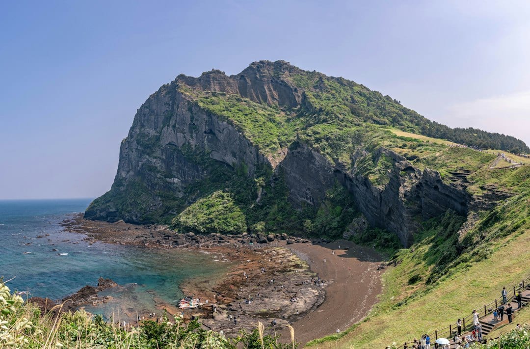 Green volcanic crater towering over the ocean and rocky shore
