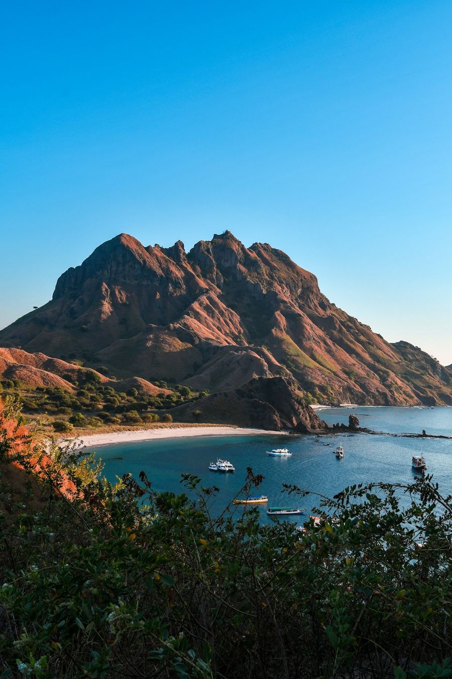 Scenic bay with boats, sandy beach, and a large mountain.