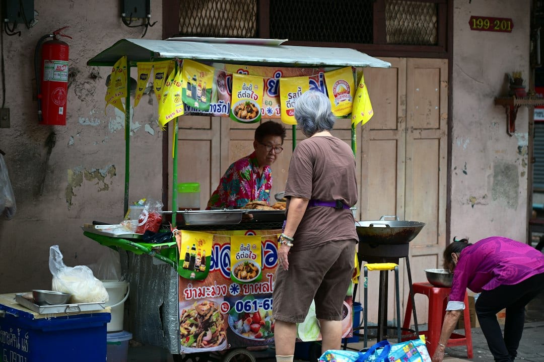 A street food vendor serving a customer at a small cart in Thailand